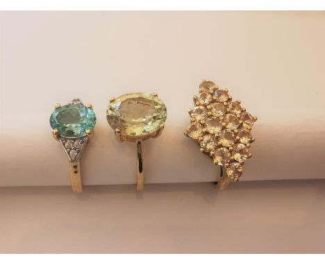 Three 20th century 10 carat yellow gold gem-set rings: a Prasiolite solitaire ring, a blue topaz flanked solitaire ring and a