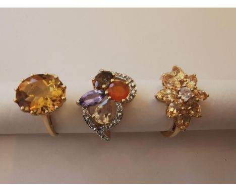 Three 20th century 10 carat yellow gold gem-set rings: a imperial topaz solitaire ring, a floral design orange and white sapp