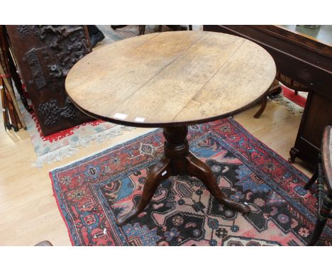 A George III oak tilt top tripod table, the circular top raised on a baluster turned column and standing on cabriole legs