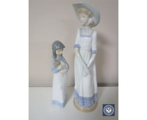 A Nao figure of a lady in a summer hat, together with another of a woman holding a dog in a blanket