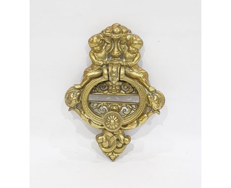 A brass door knocker cast as two putti seated above scroll work supporting a vase of fruit, the door knocker formed as a mask