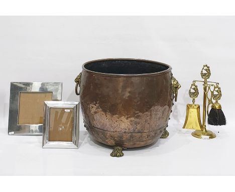 Copper cauldron on brass paw feet with lion mask and ring handles, a set of brass fireplace tools and two metal photograph fr