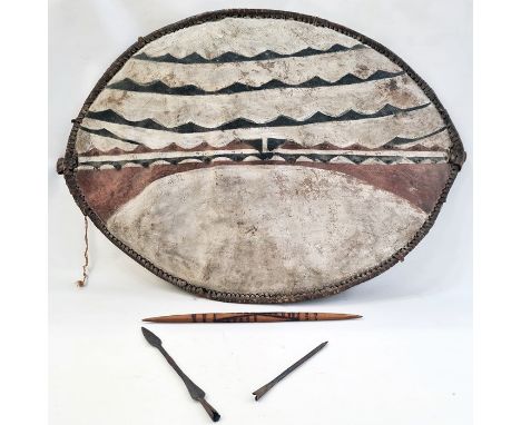 An African shield, elliptical shaped painted with white ground with black and dark red lines, two spear heads and a wooden it