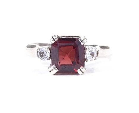 A late 20th century unmarked white metal 3-stone dress ring, stones comprising garnet and white sapphires, setting height 8.3