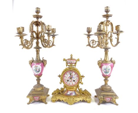 A continental ormolu clock and pair of candelabra, with enamelled dial and pink painted porcelain panels, clock height 30cm.C