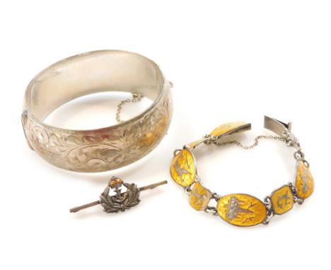 A silver bangle, floral and foliate engraved, on a snap clasp, with safety chain as fitted, Siam silver and yellow enamel bra