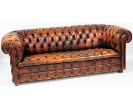 A tan leather three seater Chesterfield sofa, with button back and seat, raised on turned legs, 204cm wide. The upholstery in