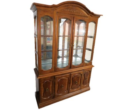 A 20thC mahogany display cabinet, the arched top with a scroll carved panel above two glazed doors, enclosing two shelves wit