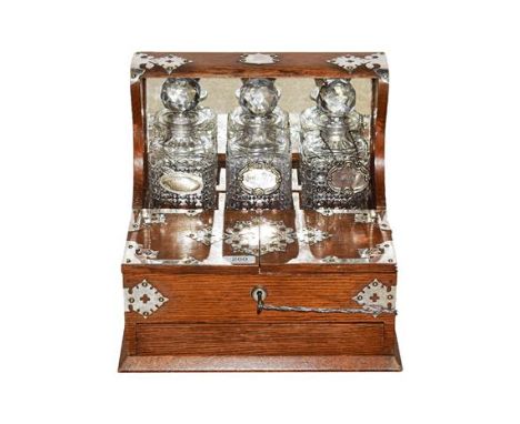 A Victorian White Metal Mounted Oak Three-Bottle Tantalus, the superstructure with shield cartouche engraved with a monogram 