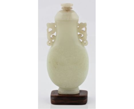 A pale green jade lidded vase with intricate flower and leaf carving to body with dragon scroll handles on wooden base, appro