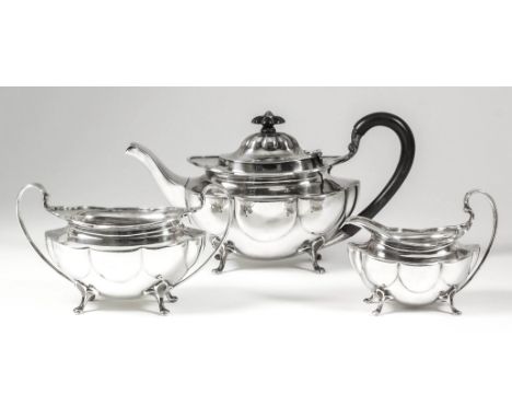An Edward VII silver oval three-piece tea service of lobed form on four scroll feet, comprising - teapot with ebonised C-scro