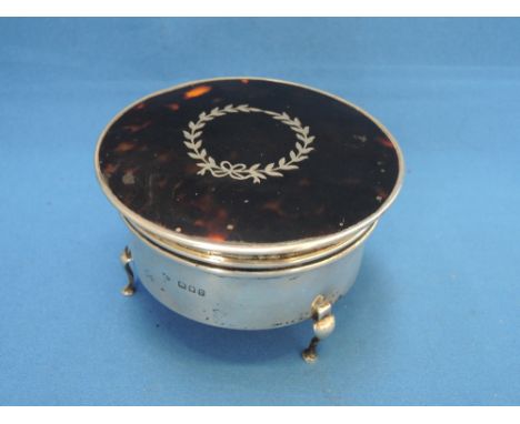 A circular silver trinket box having trefoil hoof feet, velvet lining and tortoise shell lid with inlaid silver pique leaf an