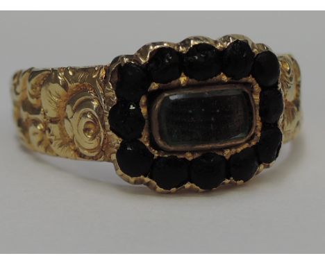 A Georgian yellow metal mourning ring having central plaited hair panel within black surround on a heavily embossed loop stam