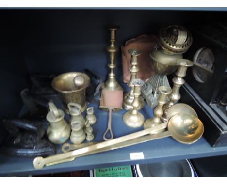 A shelf of miscellaneous metalware, including brass candlesticks, cast flat irons, copper crumb tray etc