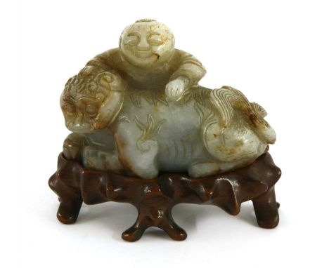 A Chinese jade carving, Ming dynasty (1368-1644), of a recumbent Buddhist lion, its fur carved in details, and a boy kneeled 