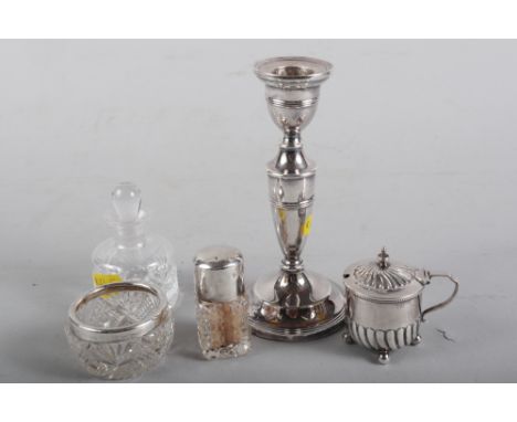 A filled silver candlestick, 6" high, a silver mustard pot with blue glass liner, a silver topped scent bottle, a silver rimm