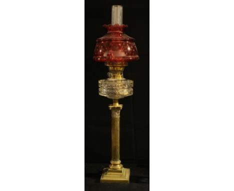 An early 20th century oil lamp, brass Corinthian column, clear glass reservoir, cranberry glass shade, 80cm high, c.1910 