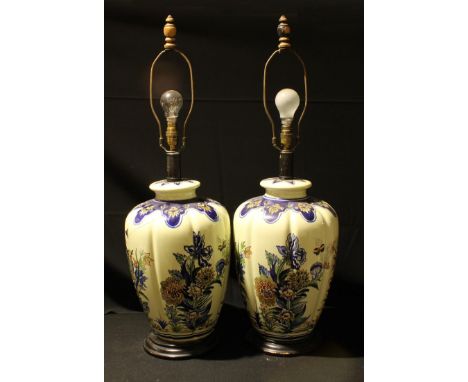 A pair of large lobed ovoid Delft style lamp bases, painted with leafy foliage, ebonised circular bases, 85cm overall 