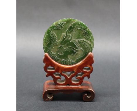 A Chinese carved jade disc depicting a dragon chasing a pearl, 6cm diameter, in a stand