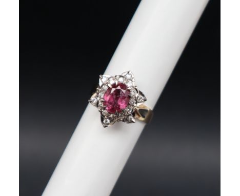 A ruby and diamond cluster ring, the central oval faceted ruby, 8mm x 7mm x 3mm deep to a white metal setting and yellow meta