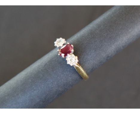 A ruby and diamond ring, set with a central oval faceted ruby flanked by a pair of round brilliant cut diamonds to a white me