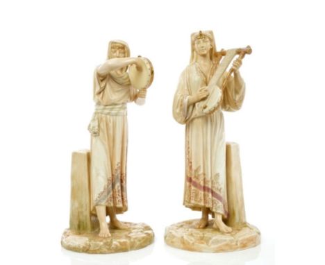 Pair of late Victorian Royal Worcester blushed ivory Egyptian revival figures modelled by Hadley, each playing a musical inst