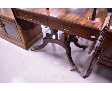 A 19th Century Regency design sofa table having beaded edge, two frieze drawers and drop flaps, over scroll supports on platf