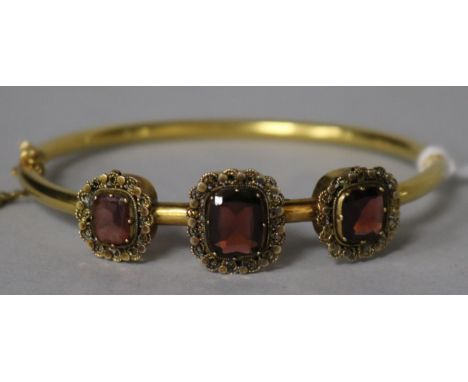 A Victorian gold and three stone garnet set hinged bangle.