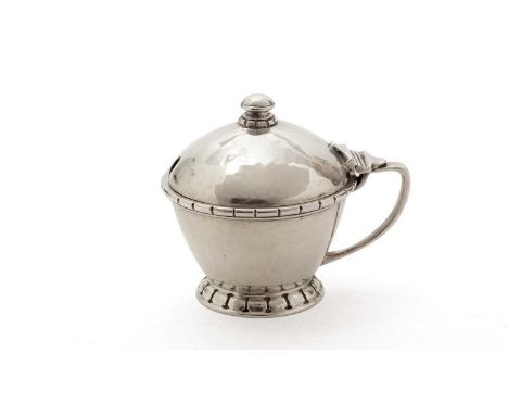 A George VI small silver mustard pot, with a hammered finish, a domed cover and notched borders, blue glass liner, by Liberty