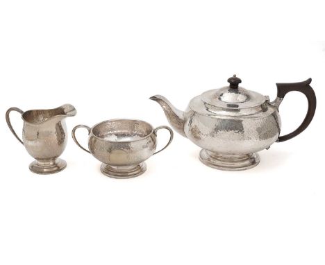 A George V silver three-piece tea set, with squat circular bodies, c-scroll handles, a hammered finish, and vacant circular c