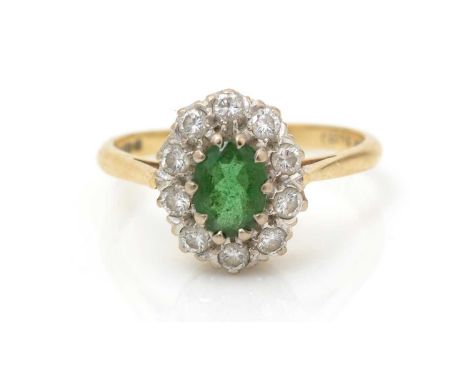 An emerald and diamond cluster ring, the oval facet cut emerald surrounded by ten brilliant-cut diamonds weighing a total of 