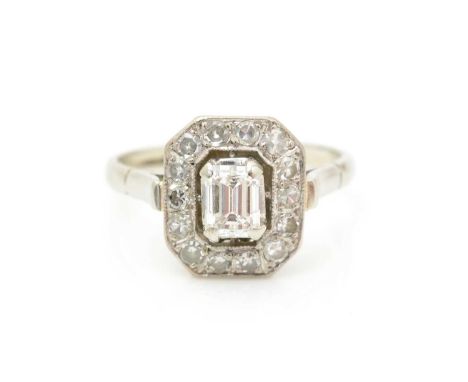 A diamond cluster ring, the central emerald-cut diamond measuring 5.2 x 4.0 x 3.5mm estimated to weigh 0.65carats, surrounded