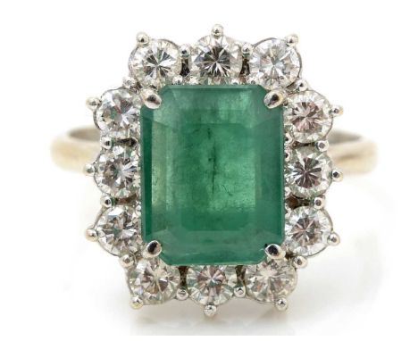 An emerald and diamond cluster ring, the central rectangular step cut emerald measuring 10.0 x 7.8 x 3.1mm estimated to weigh