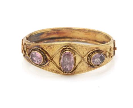 A Victorian yellow gold and quartz bangle, set with three oval facet cut quartz, foiled back with a pink hew, within twisted 