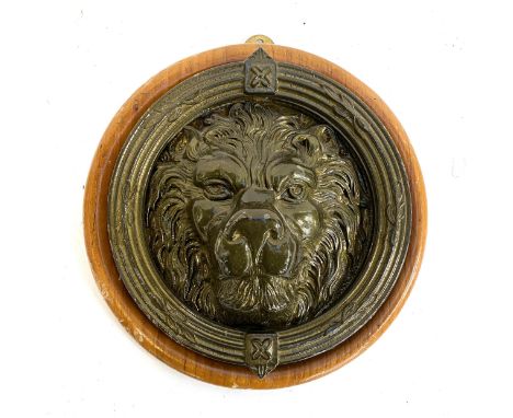 A lacquered brass lion door knocker, mounted a wooden panel, 25cmW