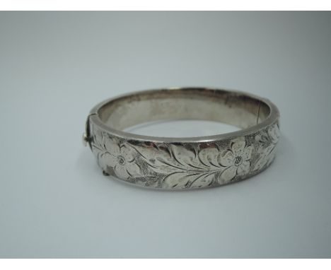 A silver hinged bangle having engraved floral decoration, safety chain missing