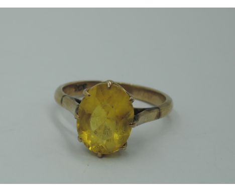 A yellow metal dress ring stamped 9ct having an oval yellow paste stone in a raised claw set mount, size P and approx 42g