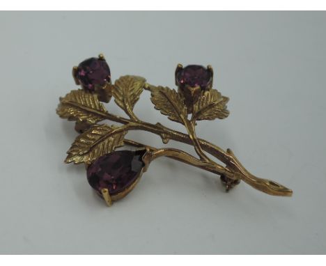 A 9ct gold brooch modelled as a sprig of flowers having a trio of amethyst style stones, approx 5.8g