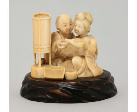 A rare ivory shunga okimono, circa 1885, of a woman pouring sake for a man as he partakes of a meal lit by a lantern, while b