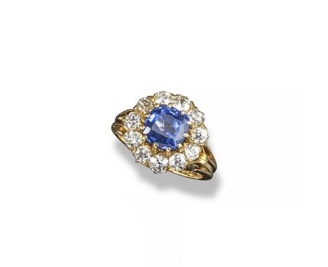 A sapphire and diamond cluster ring, the cushion-shaped sapphire is set within a surround of eleven old circular-cut diamonds