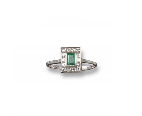An early 20th century emerald and diamond cluster ring, the baguette-shaped emerald is set within a surround of French-cut re