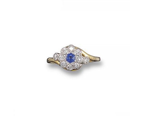 A sapphire and diamond cluster ring, the circular-cut sapphire is set within a surround of circular-cut diamonds in cross-ove