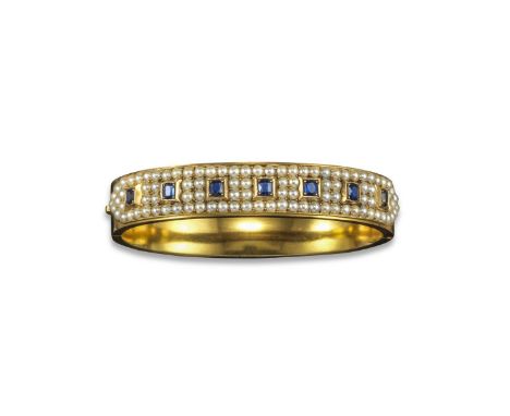 An Edwardian sapphire and seed pearl-set gold bangle, set with a line of oval-shaped sapphires within surrounds of seed pearl