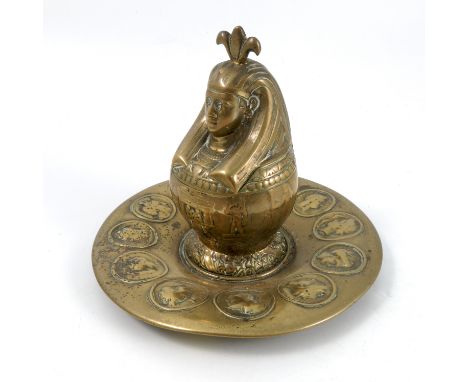 A Victorian brass inkwell, the hinged inkwell formed as an Egyptian head, on a circular dish decorated with portrait roundels