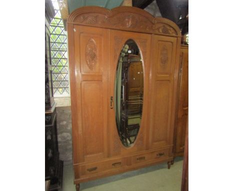 A light oak armoire with arched moulded cornice over three quarter length panelled doors, the central with oval bevelled edge