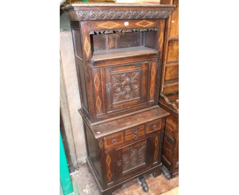 An antique oak side cupboard, the lower section enclosed by a central panel door and four small drawers, the upper section wi