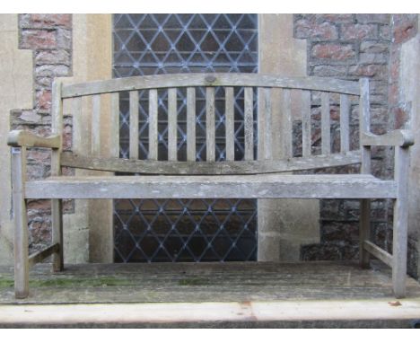 A weathered teak three seat garden bench with slatted seat and back beneath an arched rail with applied oval plaque Cannock G