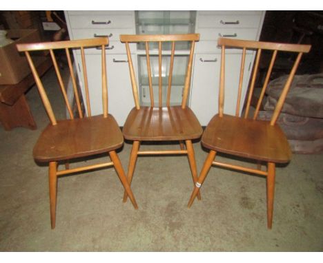 A set of three vintage Ercol light elm and beechwood dining chairs with tapered stick backs united by stretchers and splayed 