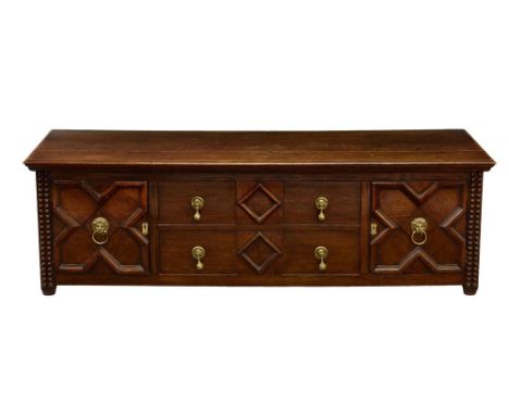 A 1920s low panelled oak chest, the moulded top over two cupboard doors with lion mask ring handles, flanking two drawers wit