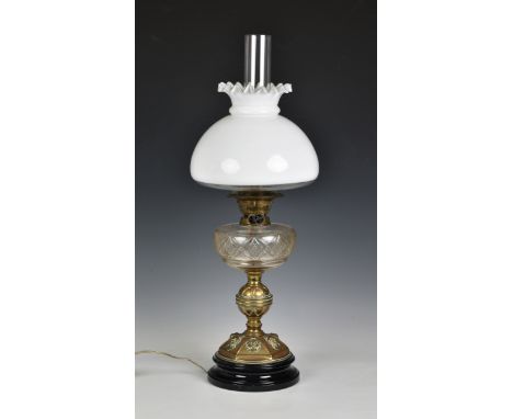 An antique brass oil lamp with electric conversion, with white milk glass shade, the brass domed base with lion mask decorati